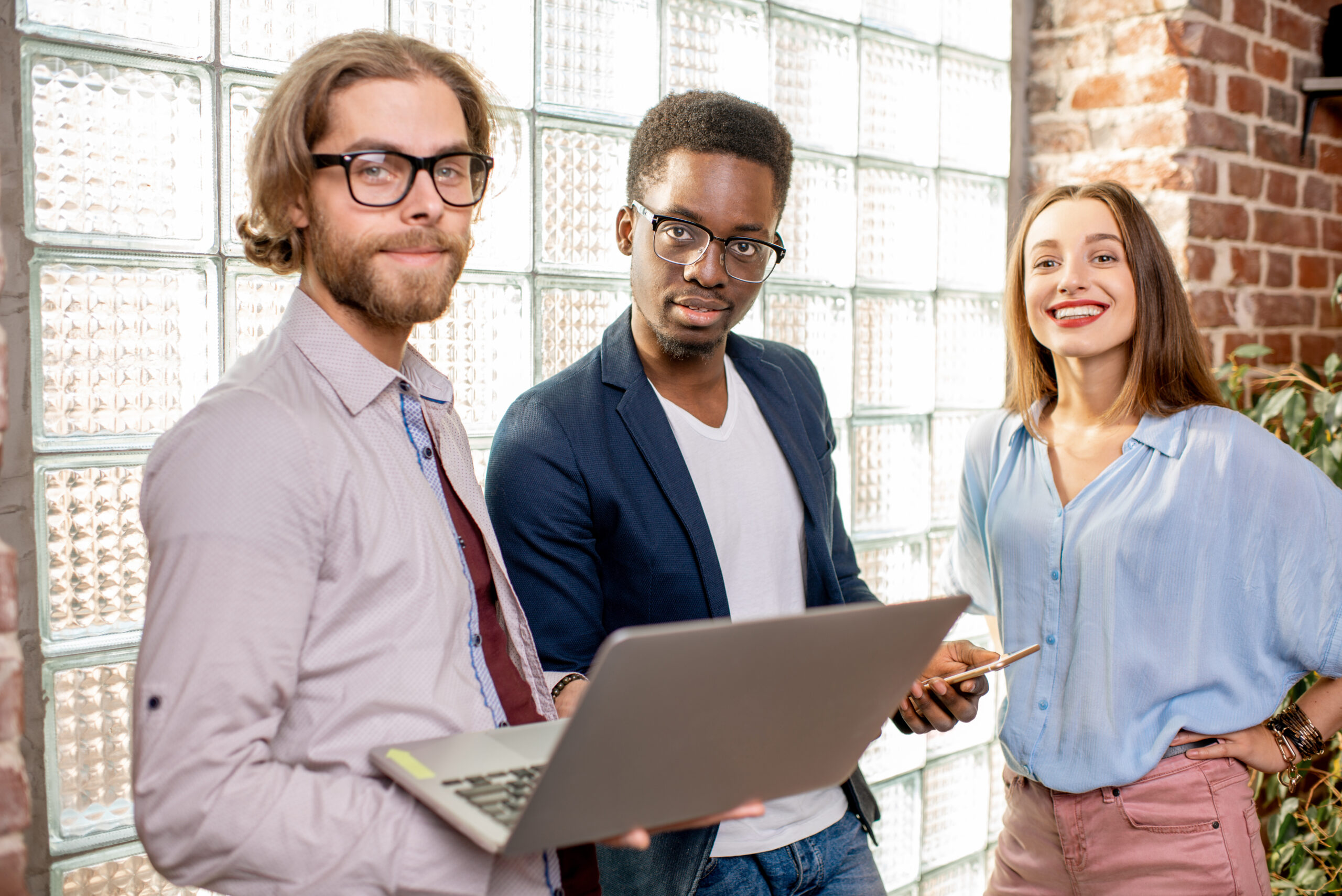 Group of young business people standing in the loft office Group of young business people dressed casually standing together near the brick wall with glass blocks indoors